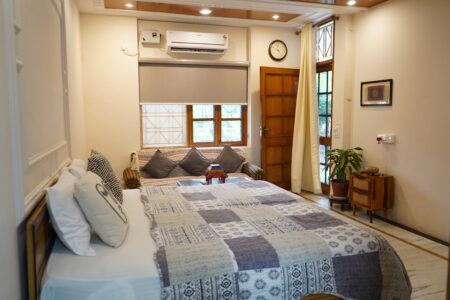 Garden-facing ground-floor room with double bed, AC, soft lighting, and wooden door at The Basera Rishikesh.