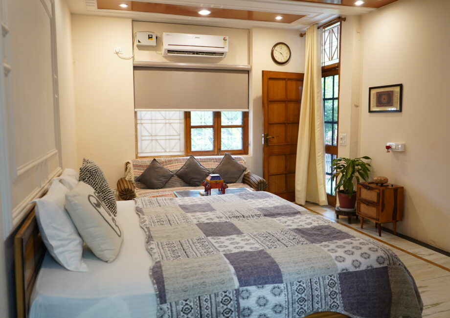 Garden-facing ground-floor room with double bed, AC, soft lighting, and wooden door at The Basera Rishikesh.