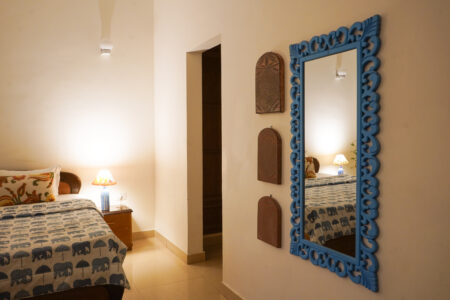 Blue carved wall mirror reflecting bed and lamp