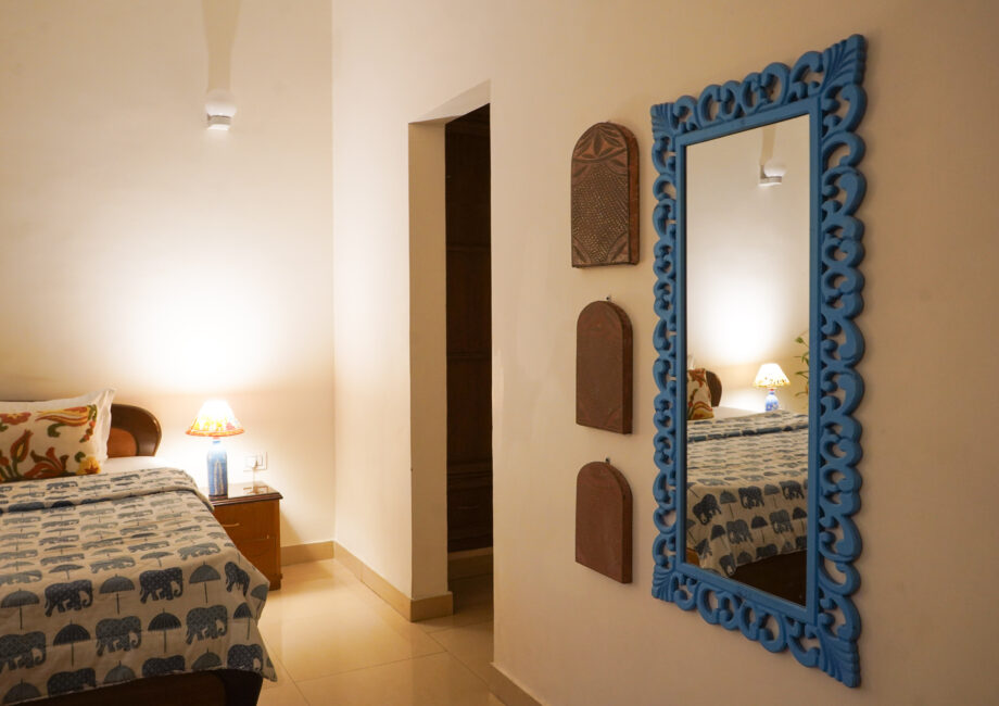 Blue carved wall mirror reflecting bed and lamp