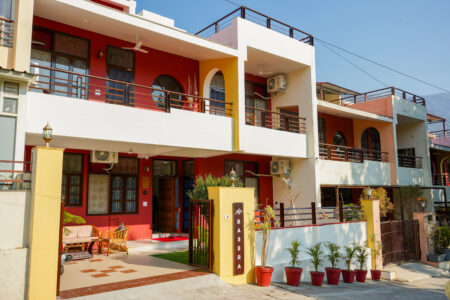 Exterior of The Basera villa with red facade, greenery and entrance gate