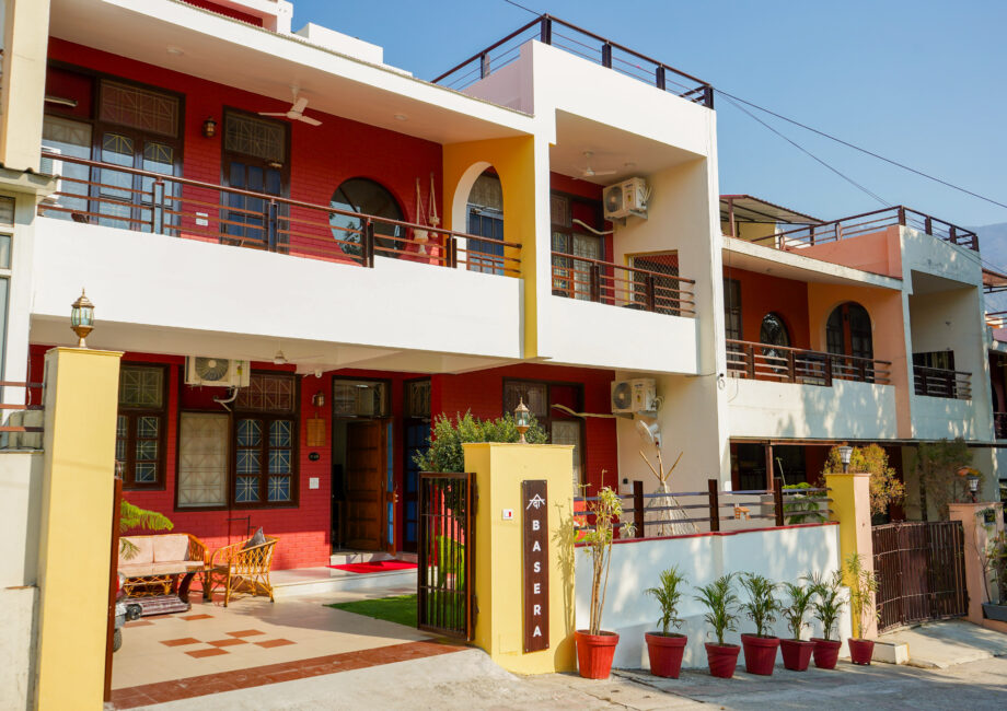 Exterior of The Basera villa with red facade, greenery and entrance gate