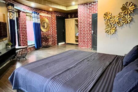 Spacious master bedroom with brick walls, blue drapes, gold wall art, and king bed at The Basera penthouse.