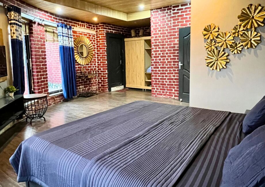 Spacious master bedroom with brick walls, blue drapes, gold wall art, and king bed at The Basera penthouse.