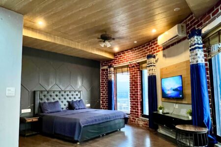 Large suite with dark accent wall, blue king bed, windows with valley view, and TV at The Basera penthouse.