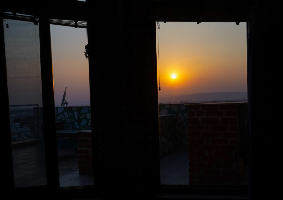 Sunset seen through glass terrace doors, with tiled patio and brick parapet silhouetted against the glowing horizon.