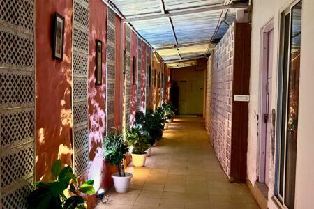 Ambient corridor with potted plants and lattice panels, warmly lit walkway at The Basera property.