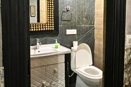 Modern bathroom with black marble walls, white vanity and gold-bead framed mirror beside a western toilet.