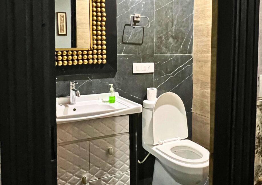 Modern bathroom with black marble walls, white vanity and gold-bead framed mirror beside a western toilet.