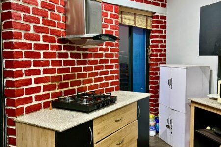 Kitchen counter with gas cooktop under a chimney hood, red brick walls, bamboo blind and storage cabinets.