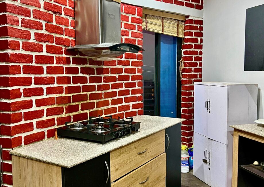 Kitchen counter with gas cooktop under a chimney hood, red brick walls, bamboo blind and storage cabinets.