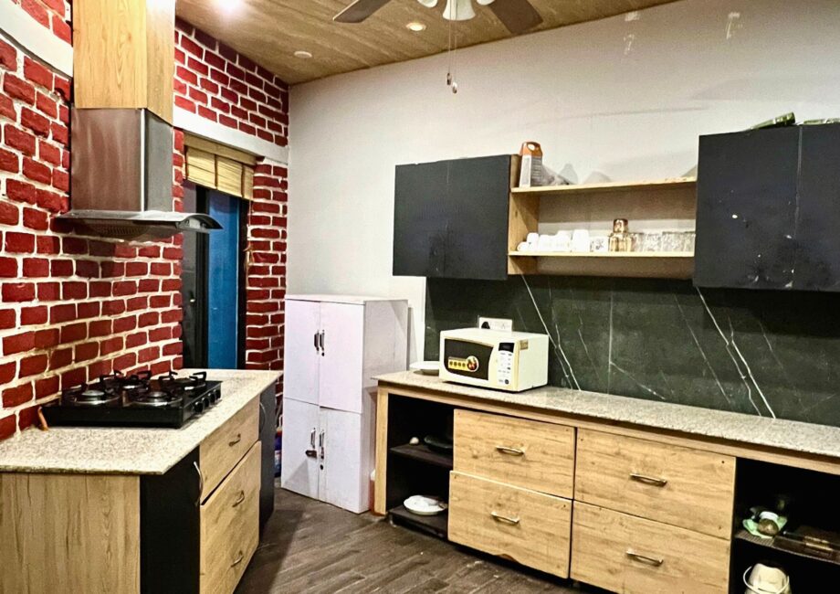 Full kitchen view with cooktop, chimney, microwave, open shelves and wood cabinets beneath a ceiling fan.