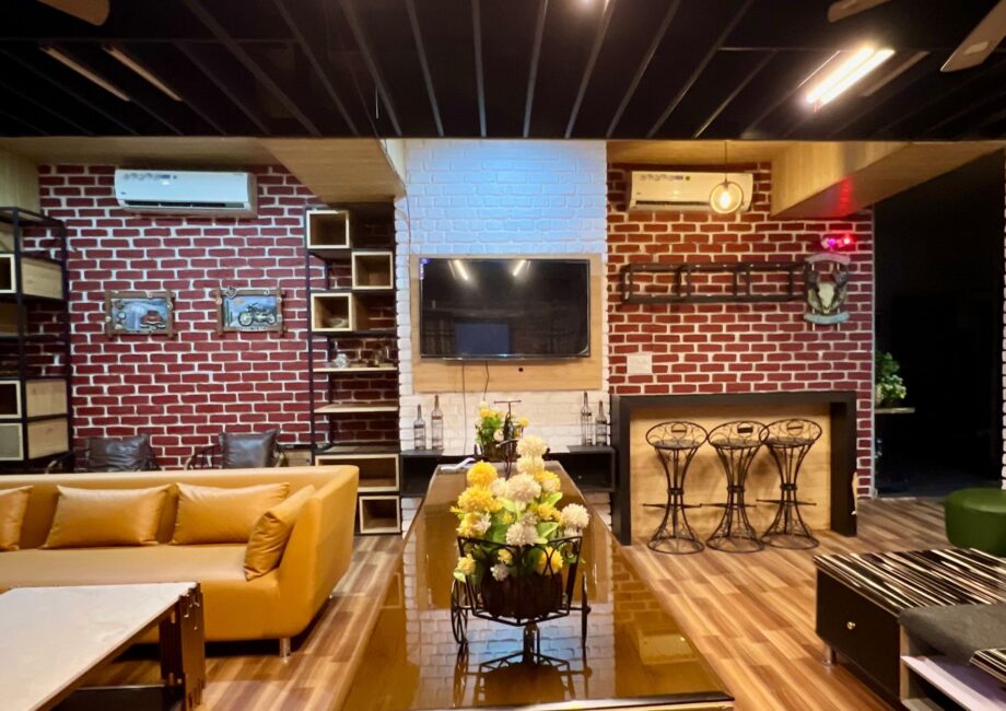Spacious living area with tan sectional, long glossy table with flower carts, brick walls and a mounted TV.