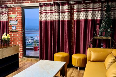 Penthouse living room with mustard sectional, maroon curtains, and terrace door facing river and hills.