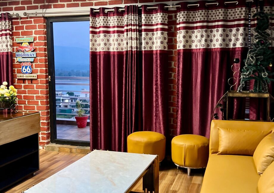 Penthouse living room with mustard sectional, maroon curtains, and terrace door facing river and hills.