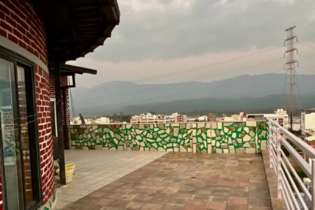 Terrace corner with mosaic parapet, mountain and forest views, and a power pylon under cloudy sky.