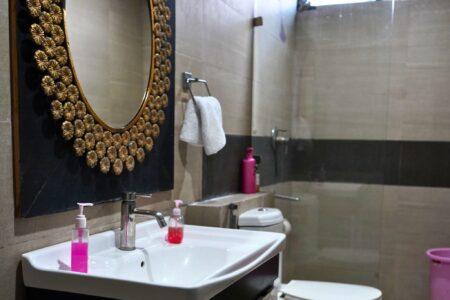 Modern bathroom with round gold-framed mirror, vanity sink, glass shower partition, and toilet at The Basera penthouse.