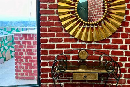 Gold sunburst mirror and wrought-iron console by a window; red brick wall and terrace outside.