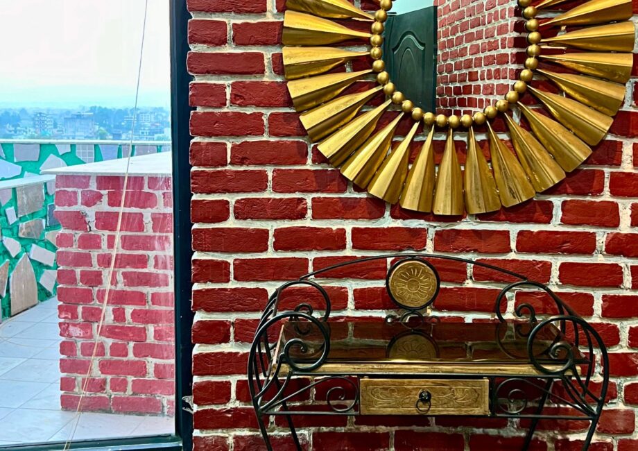 Gold sunburst mirror and wrought-iron console by a window; red brick wall and terrace outside.