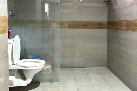 Modern bathroom with glass-partitioned shower and wall-mounted toilet, finished in large gray tiles.