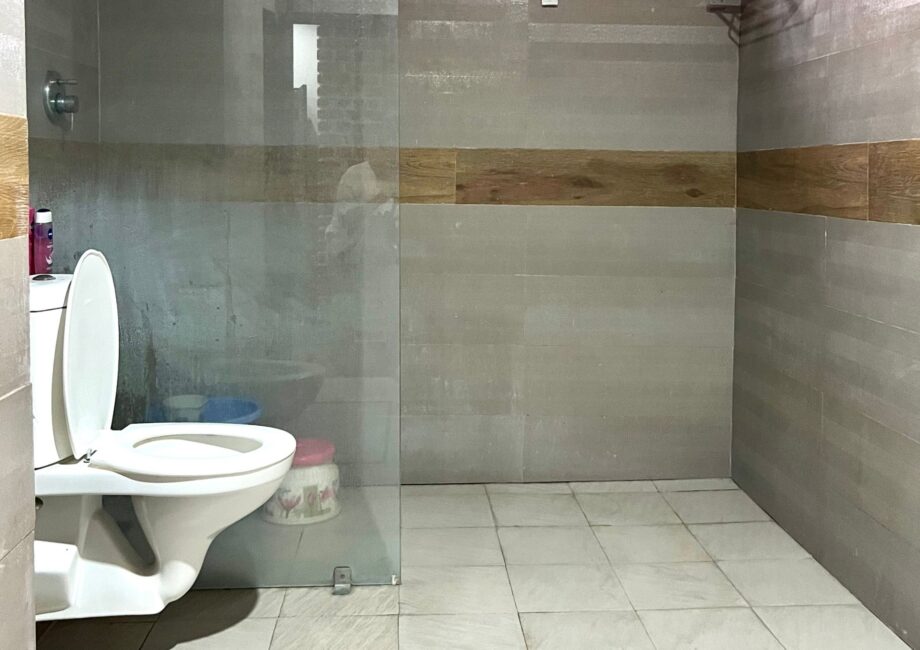 Modern bathroom with glass-partitioned shower and wall-mounted toilet, finished in large gray tiles.