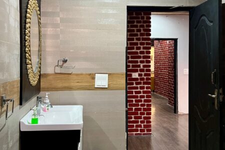 Bathroom vanity with gold-framed mirror and sink, looking out to a red-brick corridor.