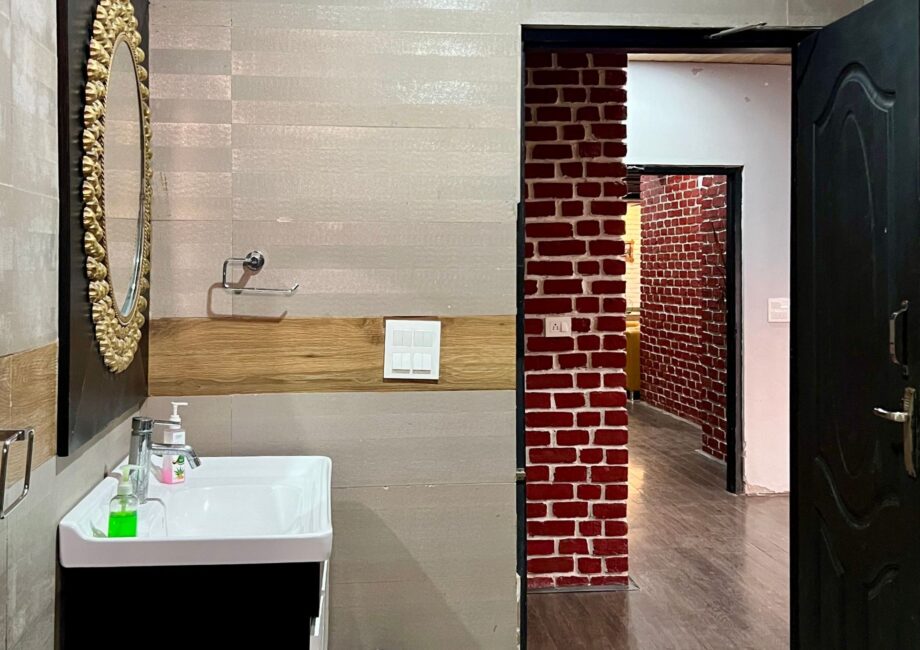 Bathroom vanity with gold-framed mirror and sink, looking out to a red-brick corridor.