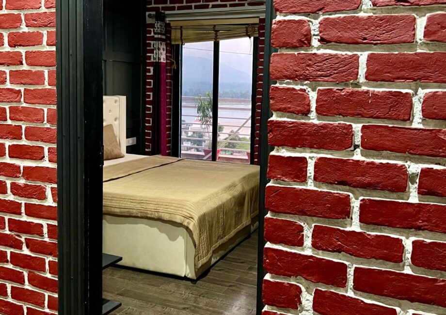 Bedroom with balcony and river–mountain view framed by red brick walls at The Basera penthouse.