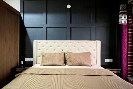 King bed with cream tufted headboard against charcoal feature wall, tan bedding at The Basera penthouse.