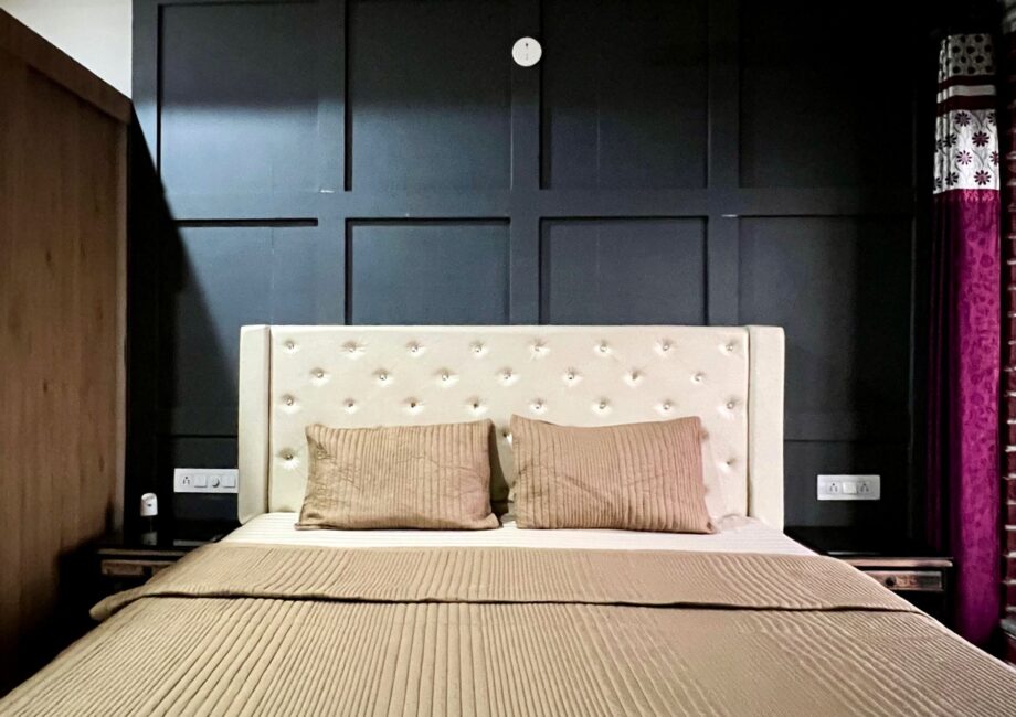 King bed with cream tufted headboard against charcoal feature wall, tan bedding at The Basera penthouse.