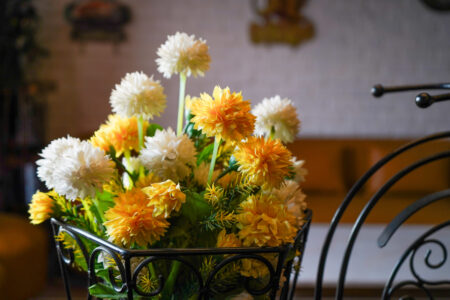 Close-up of yellow and white flower arrangement in wrought-iron basket with lounge in background