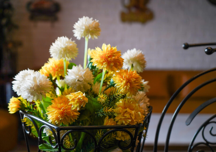Close-up of yellow and white flower arrangement in wrought-iron basket with lounge in background