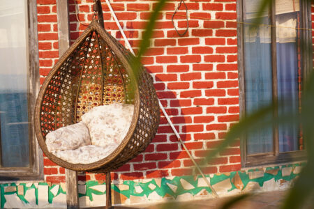 Hanging rattan egg chair on the penthouse terrace against red-brick wall and sliding window