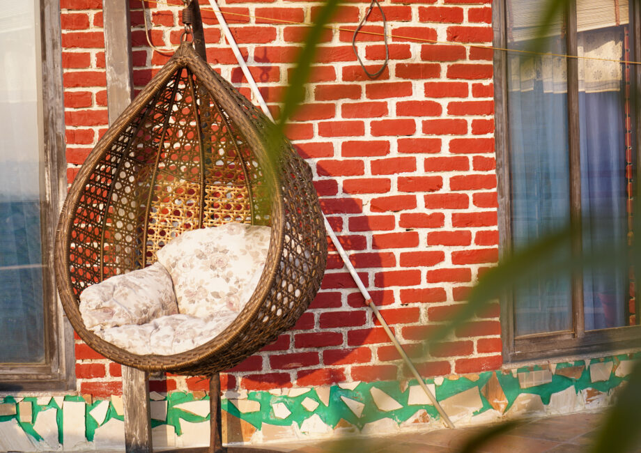 Hanging rattan egg chair on the penthouse terrace against red-brick wall and sliding window