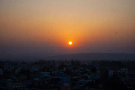 Vibrant orange sunset over a city skyline with distant rolling hills under a clear evening sky.