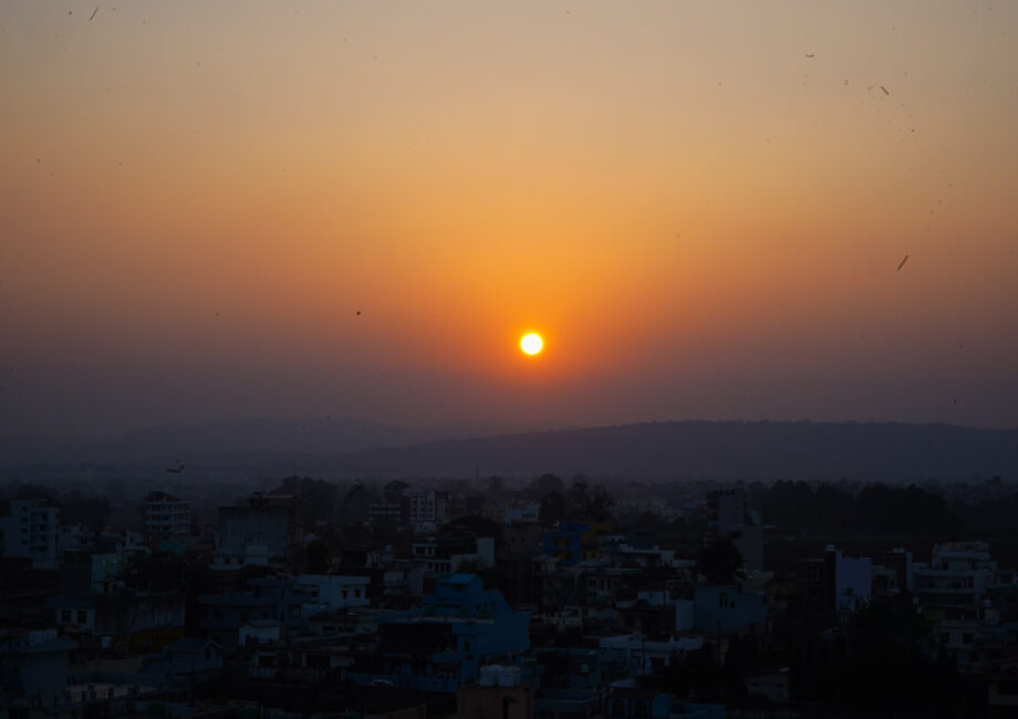 Vibrant orange sunset over a city skyline with distant rolling hills under a clear evening sky.