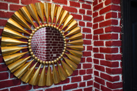 Decorative gold sunburst wall mirror mounted on a red brick feature wall, close-up detail.