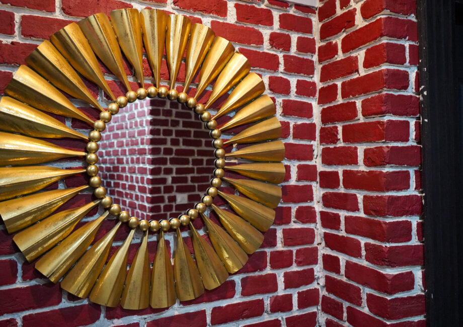 Decorative gold sunburst wall mirror mounted on a red brick feature wall, close-up detail.