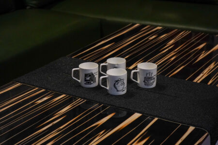 Black striped coffee table with four white mugs in front of a green sectional sofa.