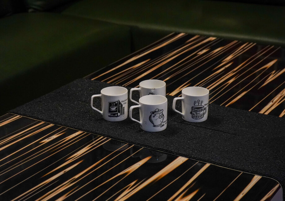 Black striped coffee table with four white mugs in front of a green sectional sofa.