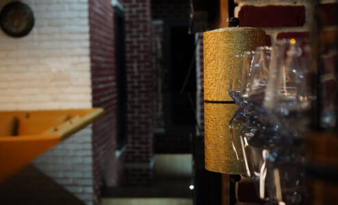 Bar detail showing gold ice bucket and hanging stemware, with brick-loft lounge blurred behind.