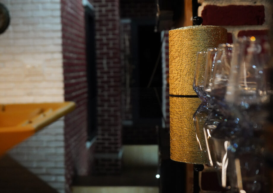 Bar detail showing gold ice bucket and hanging stemware, with brick-loft lounge blurred behind.