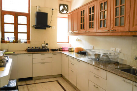 Fully equipped modern kitchen with gas stove, chimney, and natural light through wooden-framed windows