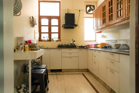 Fully equipped modern kitchen with gas stove, chimney, and natural light through wooden-framed windows
