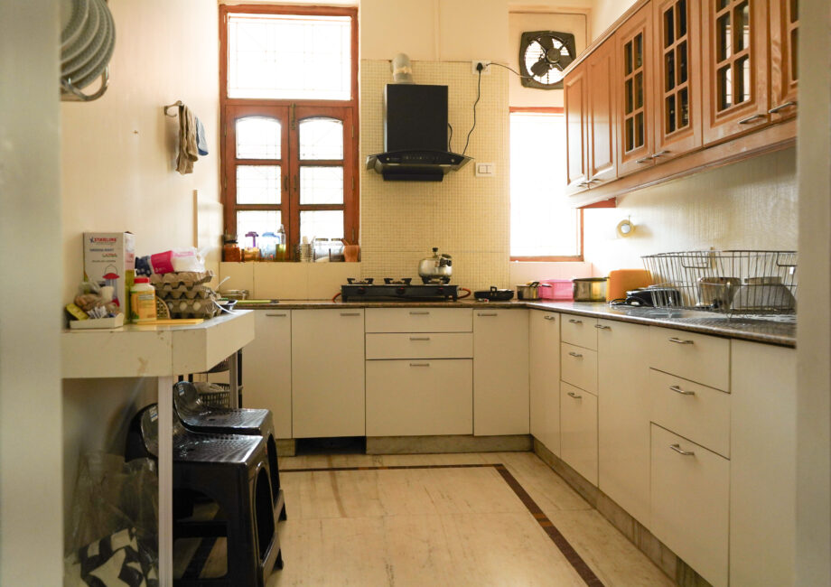Fully equipped modern kitchen with gas stove, chimney, and natural light through wooden-framed windows