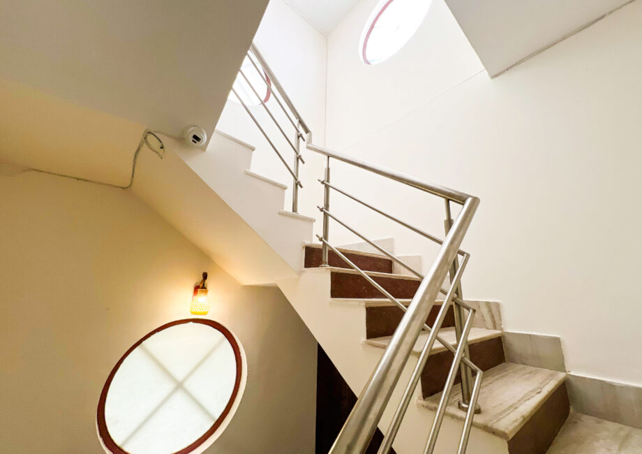 Bright indoor staircase with circular frosted glass window and clean railing in The Basera 4BHK villa